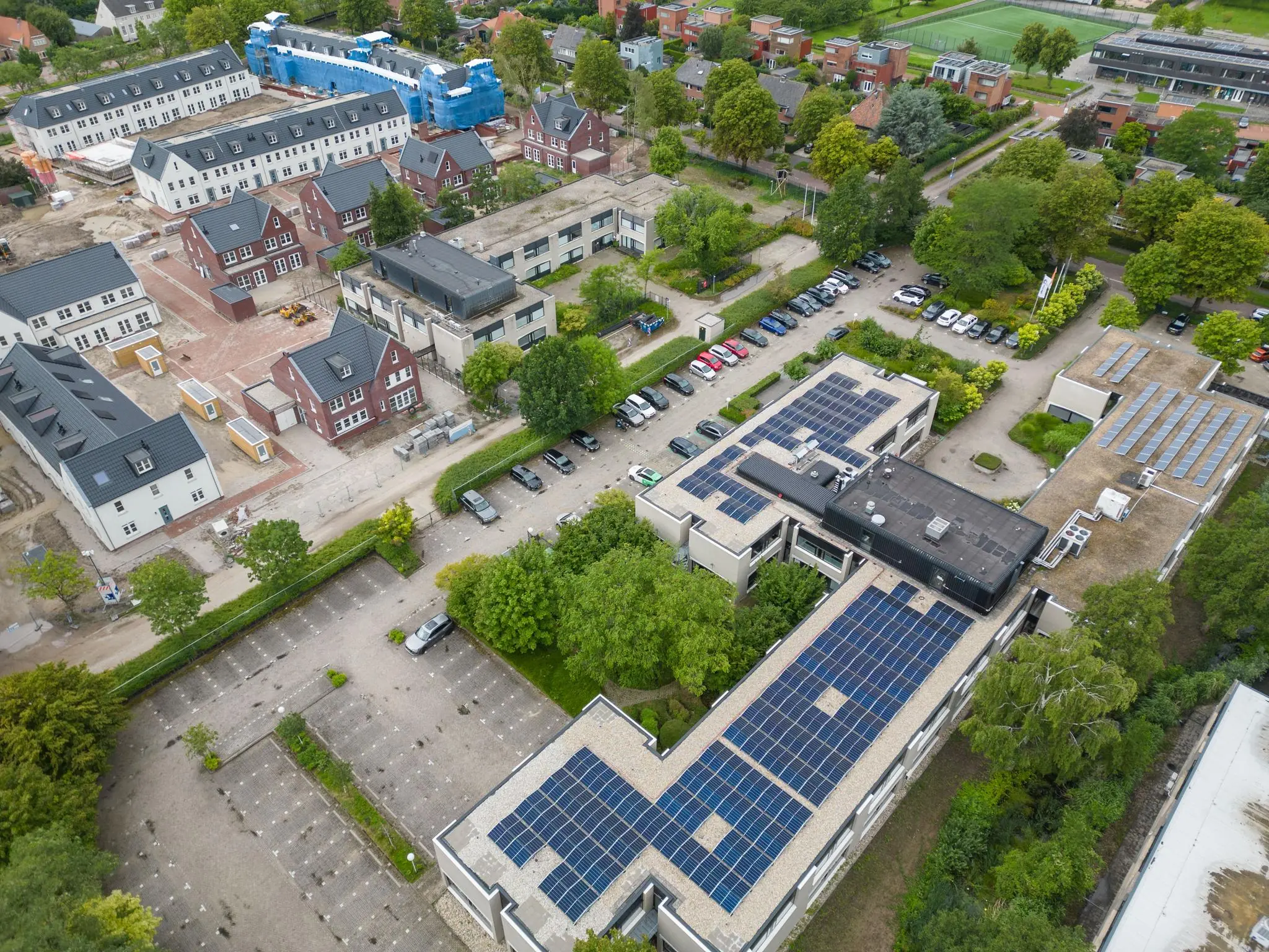 Luchtfoto van gebouwen aan de Burgemeester Verderlaan, met zonnepanelen op daken en een nieuwbouwwijk in aanbouw.